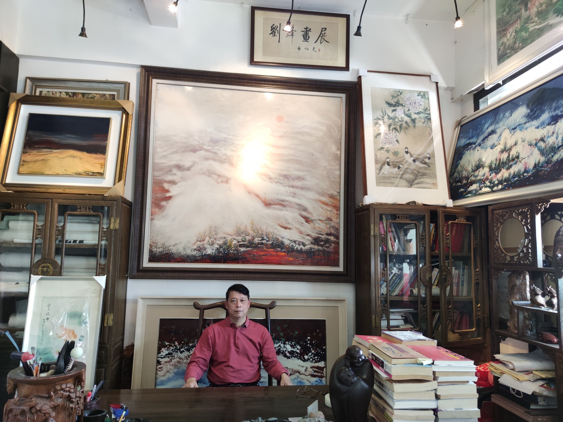 刘烽坐在画廊中，身后陈列作品与书籍